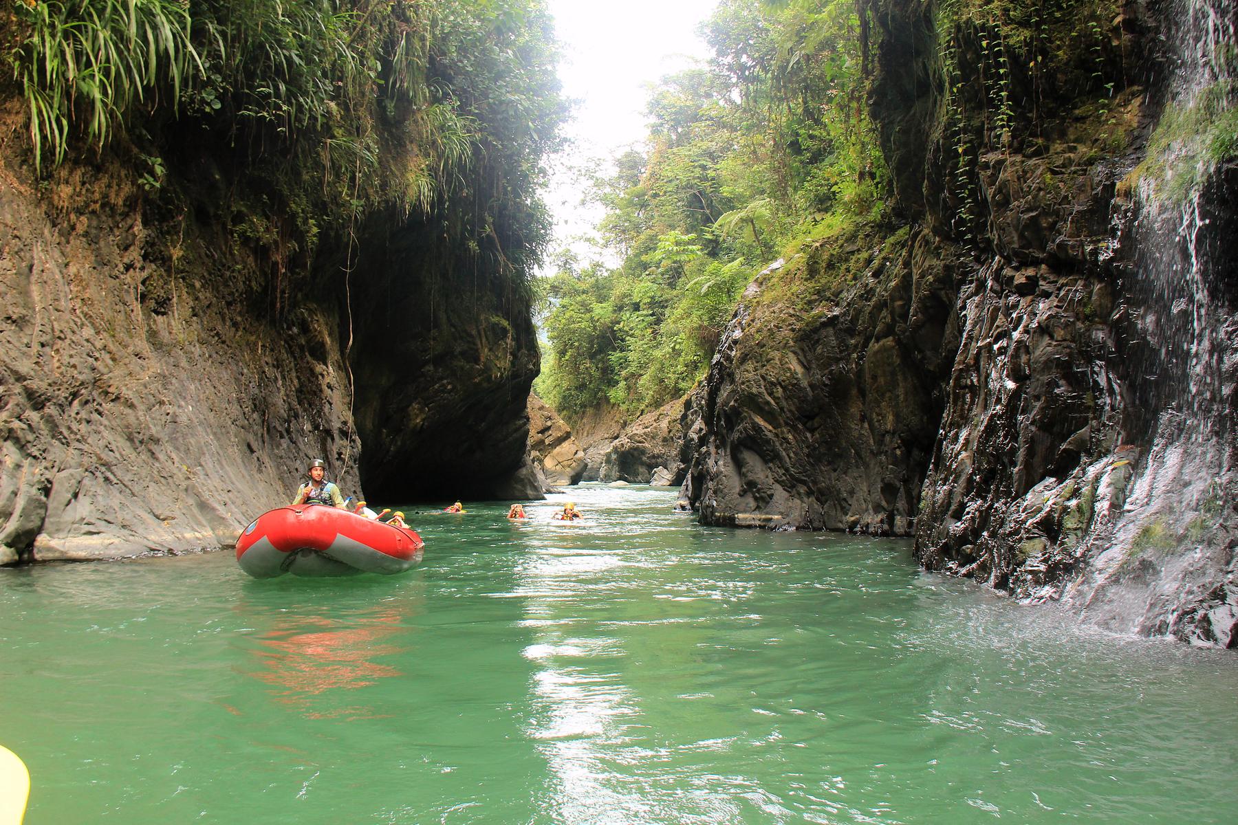 A raft in the green pool of the Chorro canyon, with a waterfall on the rock wall
