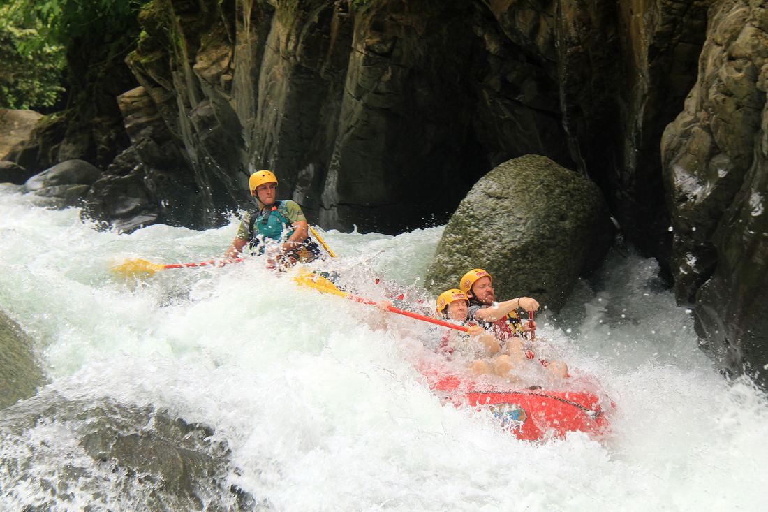 A raft punching through a hole beside a boulder in the Chorro canyon